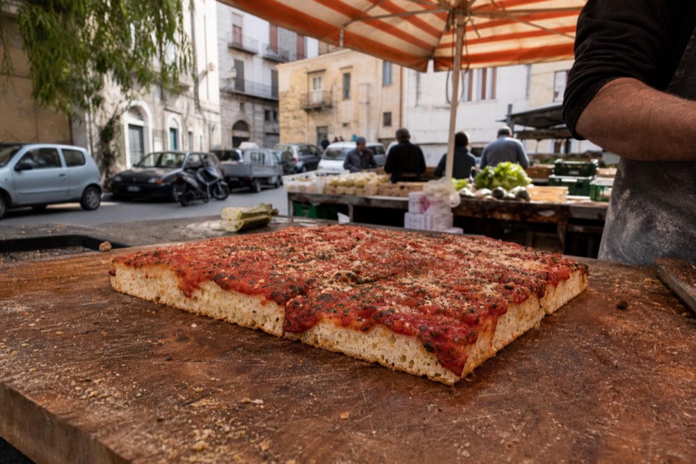 A slice of sfincione on a wooden counter at a Palermo market stall