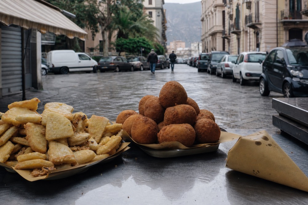 Fried arancine and panelle stacked on a market food counter