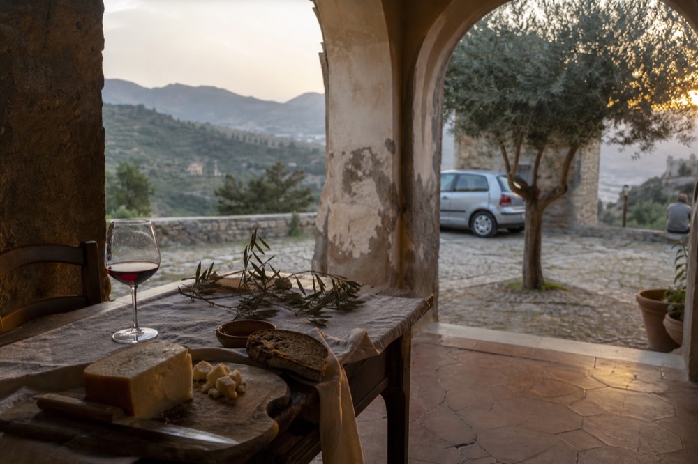A rustic table with Sicilian dishes, bread and a glass of red wine