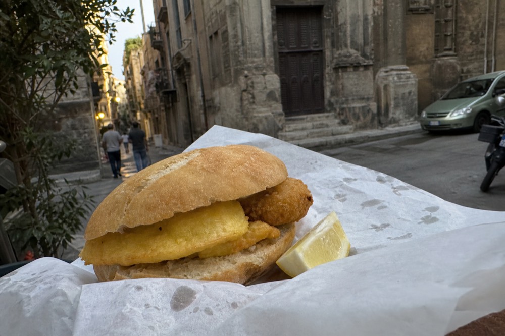 A freshly made panelle and crocche sandwich on a rustic roll with a wedge of lemon