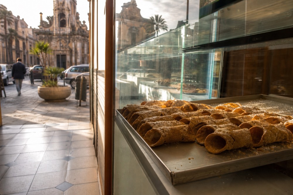 Rows of unfilled cannolo shells arranged on a tray in a pastry shop window