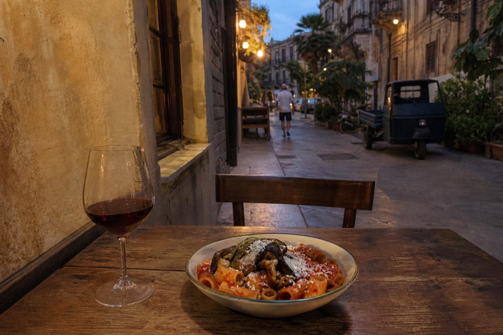 Bowl of pasta with fried aubergine, tomato sauce and grated ricotta salata on a rustic table