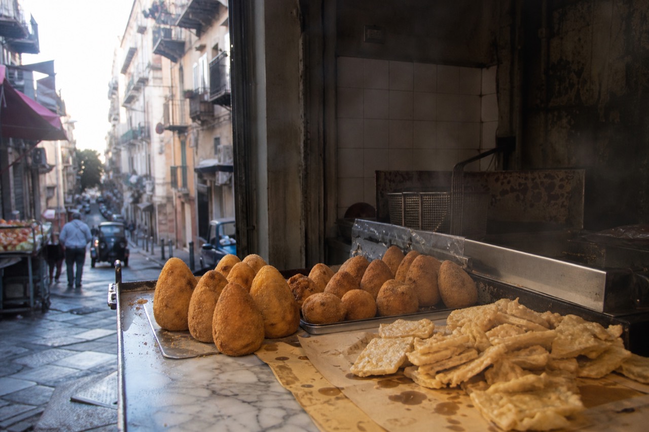 Fried arancine and chickpea panelle arranged on a marble market counter in Palermo