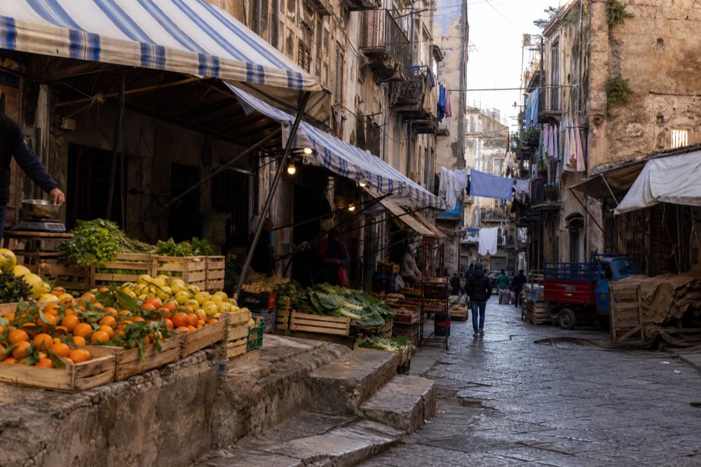 A busy Palermo market lane with produce stalls and awnings under morning light