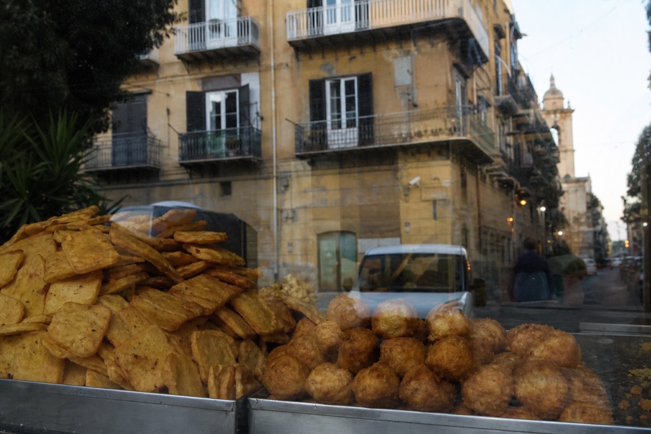 Freshly fried chickpea fritters and rice balls stacked in a Palermo street food shop window