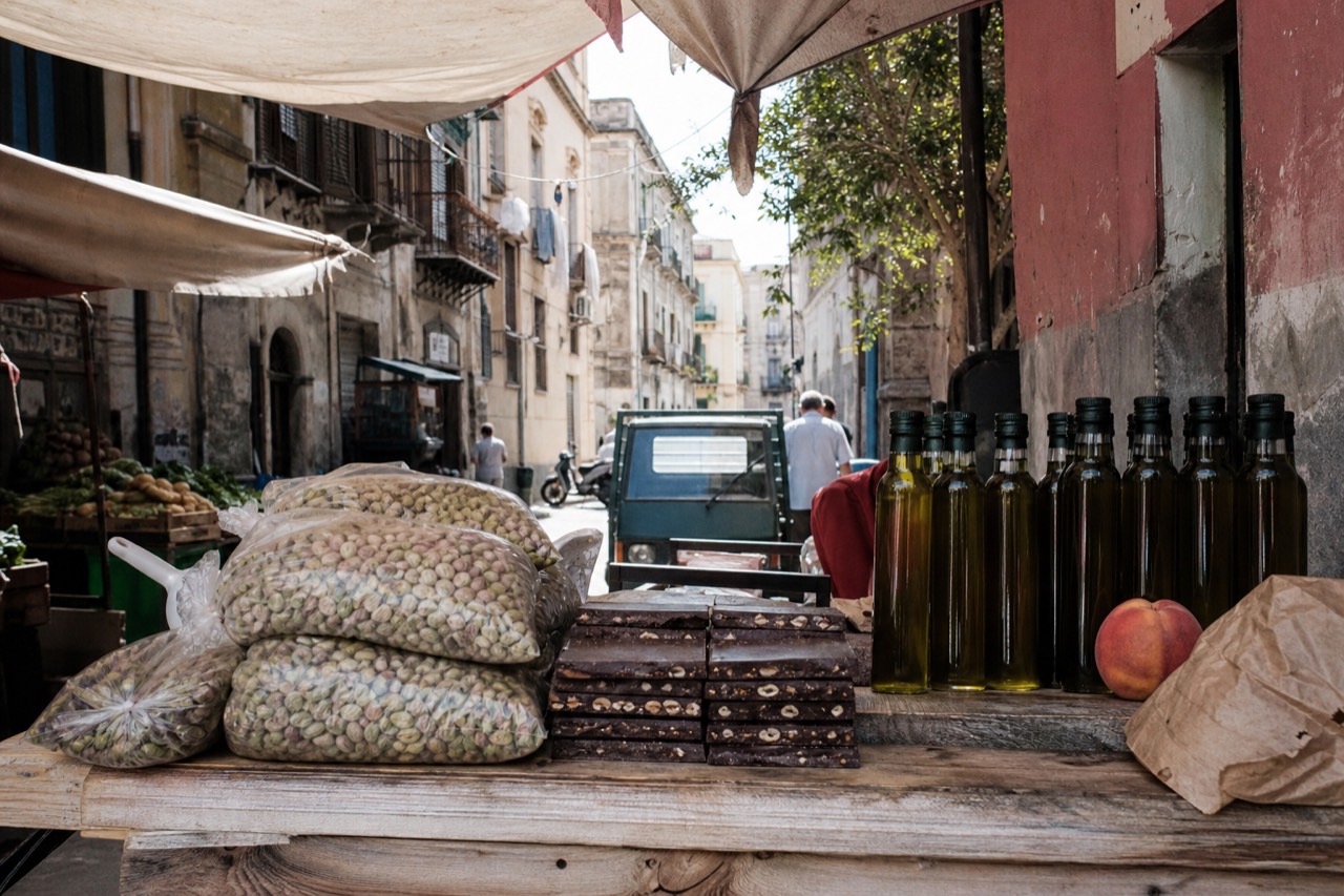Sicilian pistachios, chocolate bars and bottles of olive oil arranged on a wooden market counter