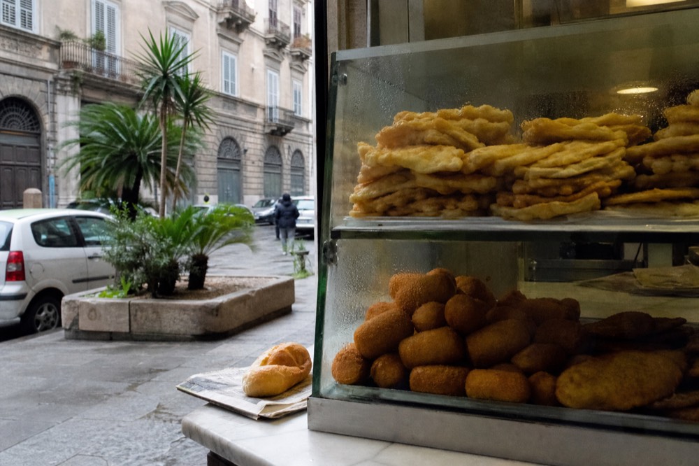 Fried chickpea fritters and potato croquettes stacked at a Palermo street food counter