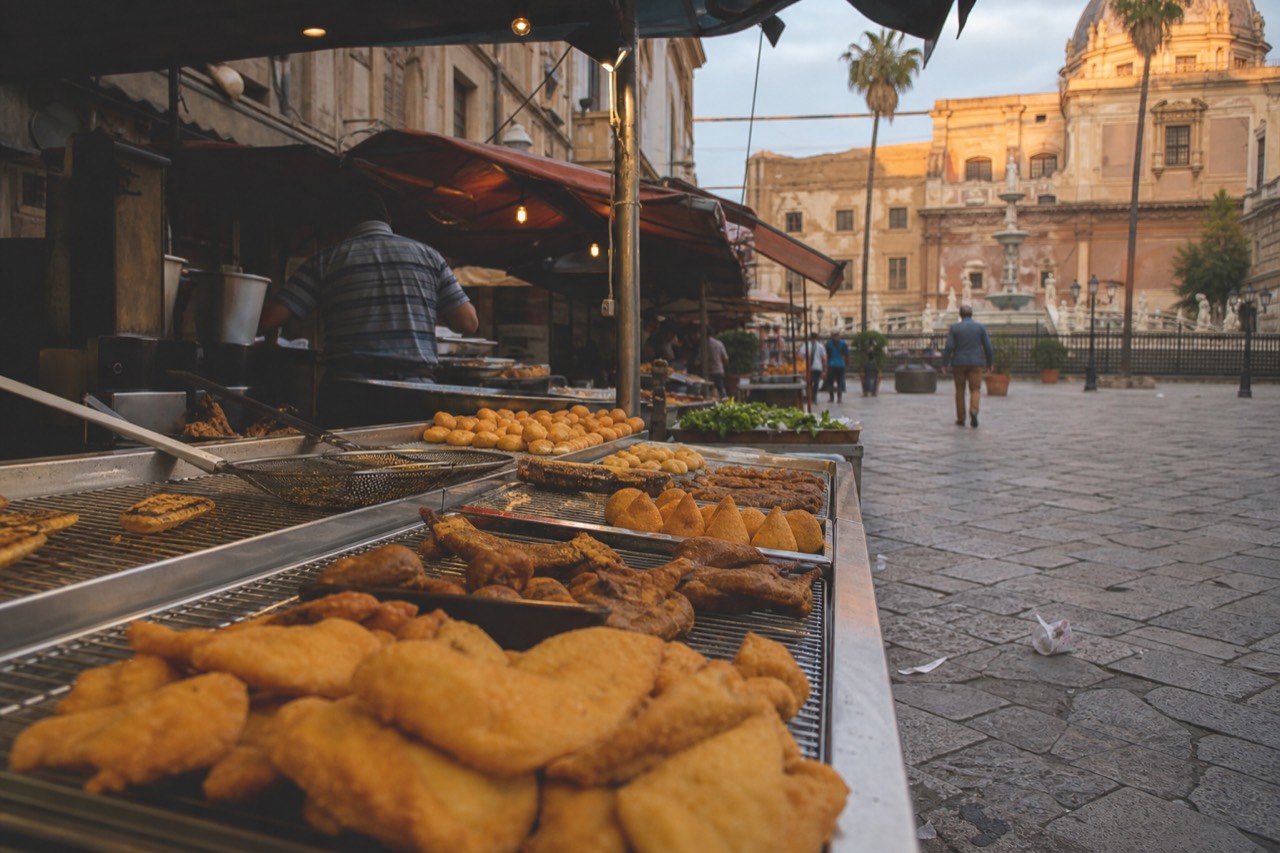 Sicilian street food stall with fried snacks and market awnings in an old city square