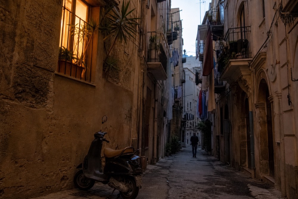 A narrow Palermo alley with tall stone buildings, laundry lines and soft evening light