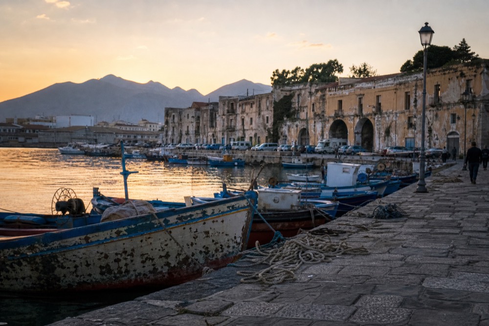 Fishing boats and stone harbour buildings along the Palermo waterfront at sunset