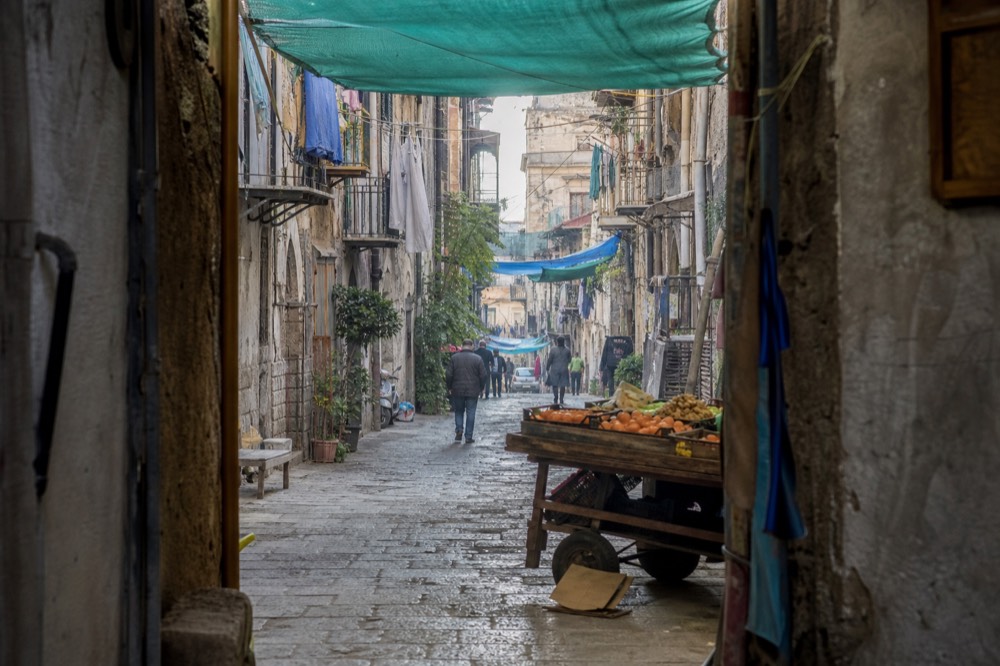 Narrow market street with hanging canopies and painted shop signs in the Albergheria quarter