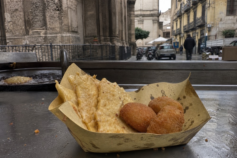 Fried chickpea fritters and potato croquettes served in a paper tray