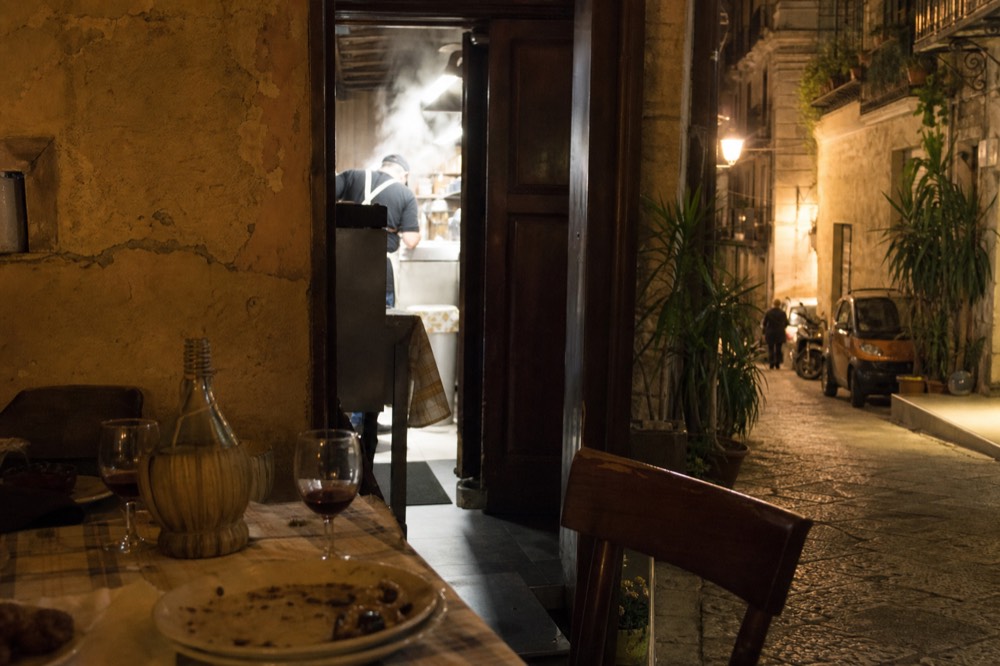 A laid table with white plates, glasses of red wine and a carafe in a small trattoria room