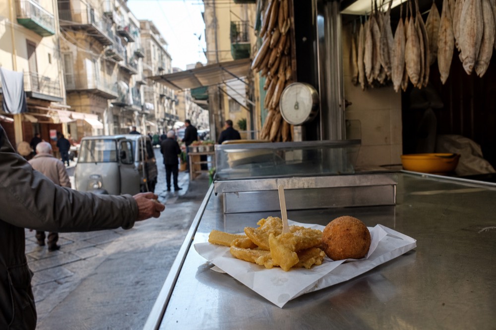 Fried chickpea fritters and a rice ball served on paper at a market counter