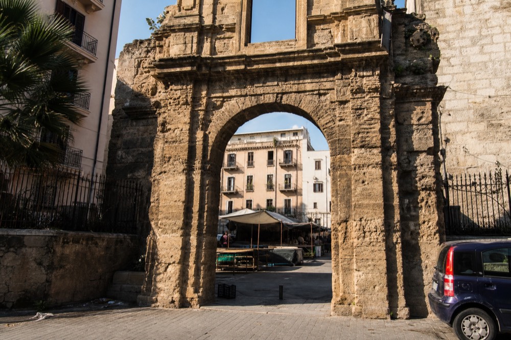 An old stone gate in Palermo with market streets visible beyond it