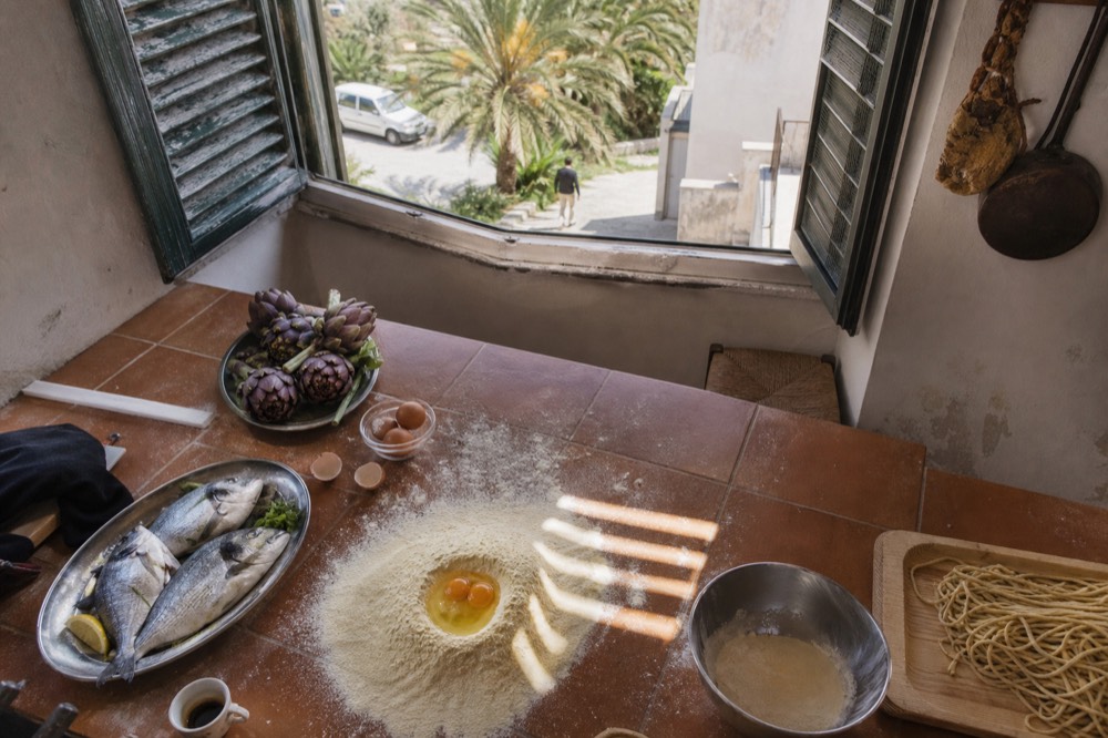 A kitchen counter with fresh vegetables, fish and pasta ingredients laid out for a cooking class