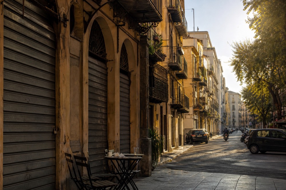 A Palermo street corner in late afternoon with cafe tables and closed market shutters