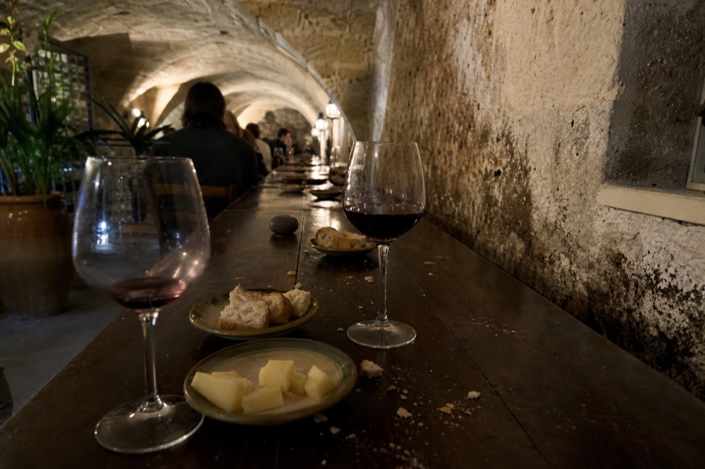 Glasses of red wine and small plates of cheese arranged on a wooden tasting table