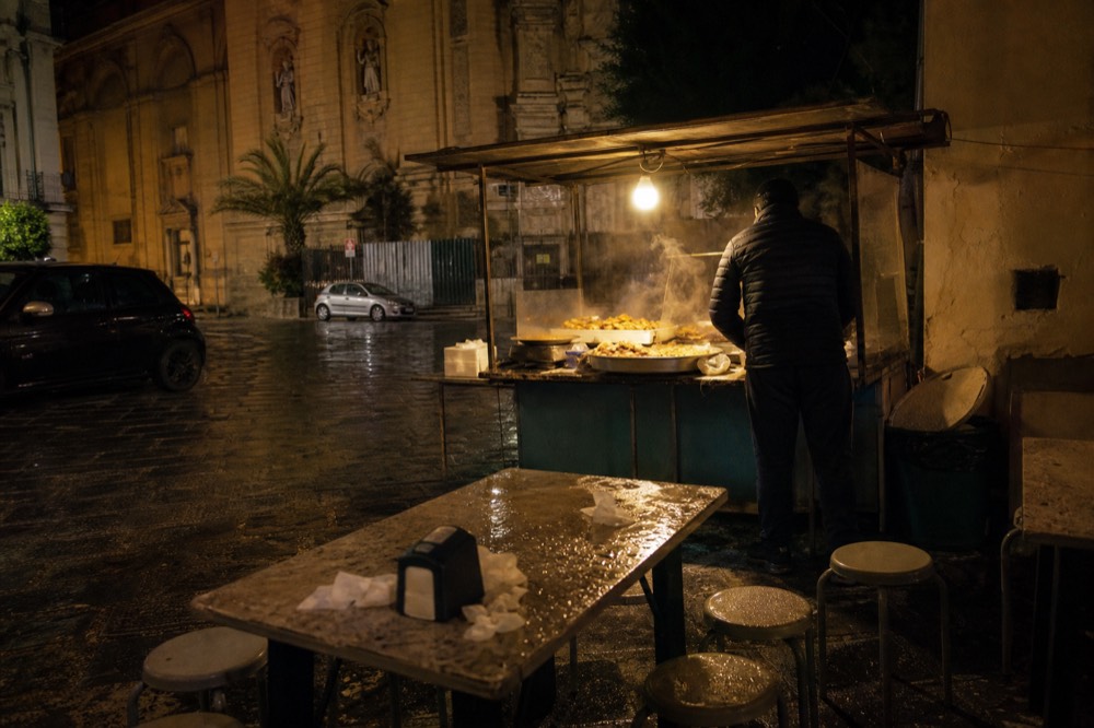 An evening street food stall glowing under lights with trays of fried snacks