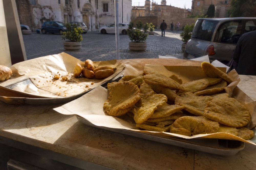 Fried chickpea fritters and potato croquettes stacked at a Palermo food counter