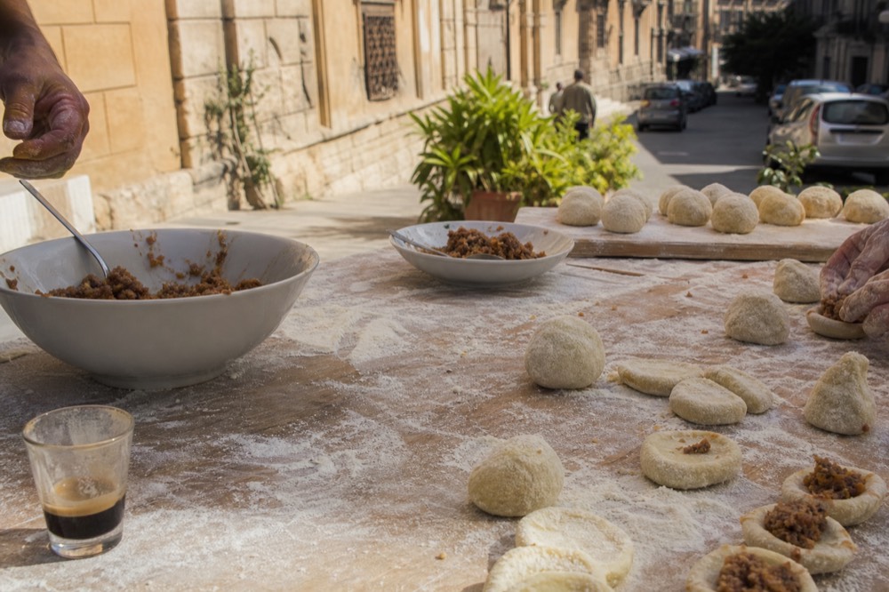 Hands shaping rice balls on a floured wooden board beside bowls of filling