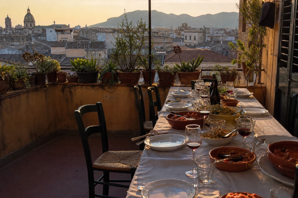 A long kitchen table set for a group meal with wine glasses and serving dishes