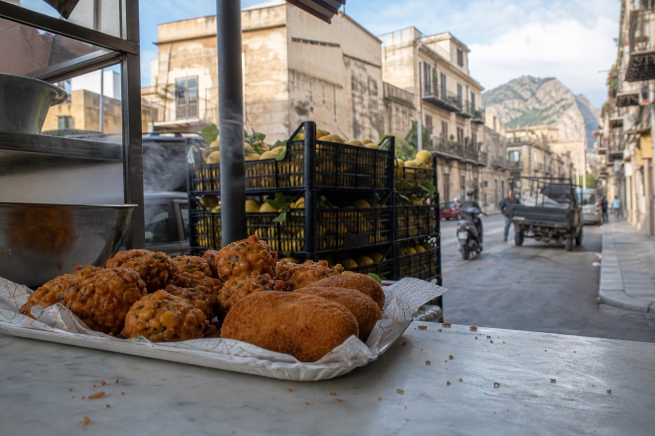 Fried chickpea fritters and potato croquettes in a paper tray on a marble market counter in Palermo