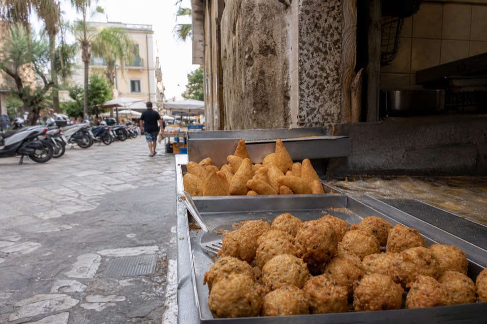 Evening crowd eating and drinking in the Vucciria, with sfincione and stigghiola stalls lit up