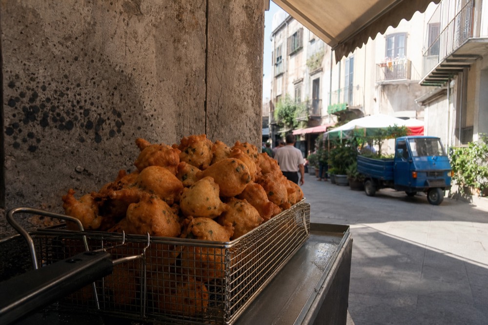 Golden chickpea fritters stacked in a fryer basket at a Palermo market stall