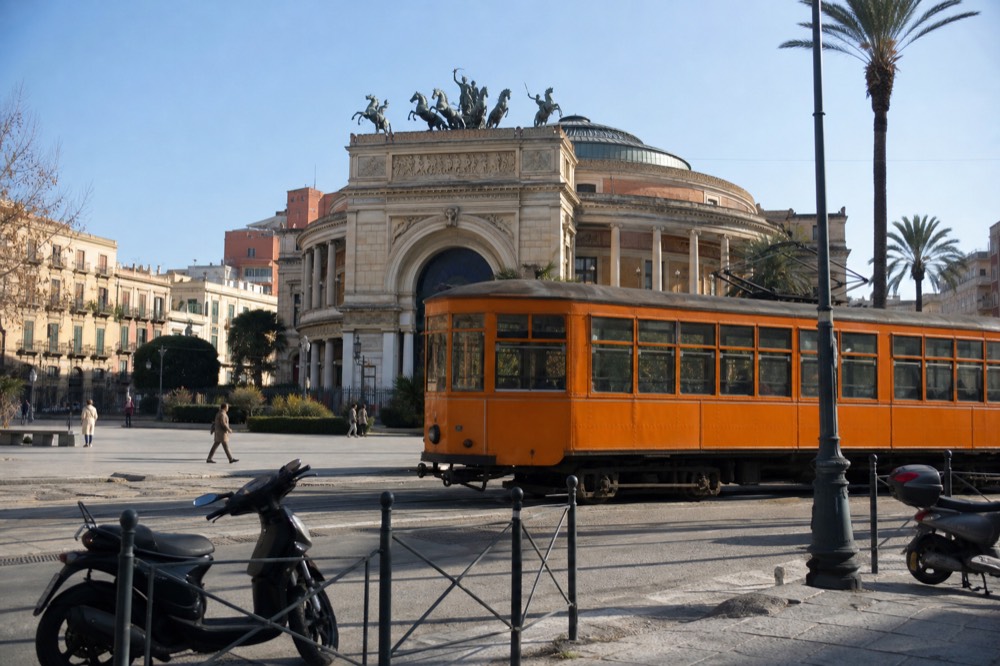 A Palermo street with a historic tram and pedestrians near the opera house