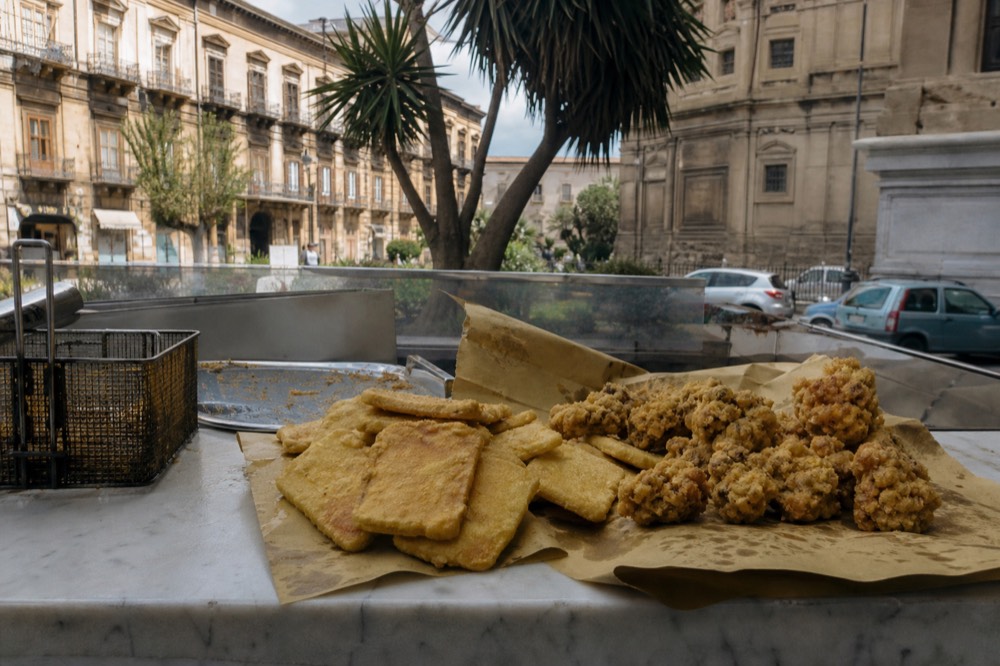 Fried golden panelle and chickpea fritters stacked in paper at a Palermo street counter