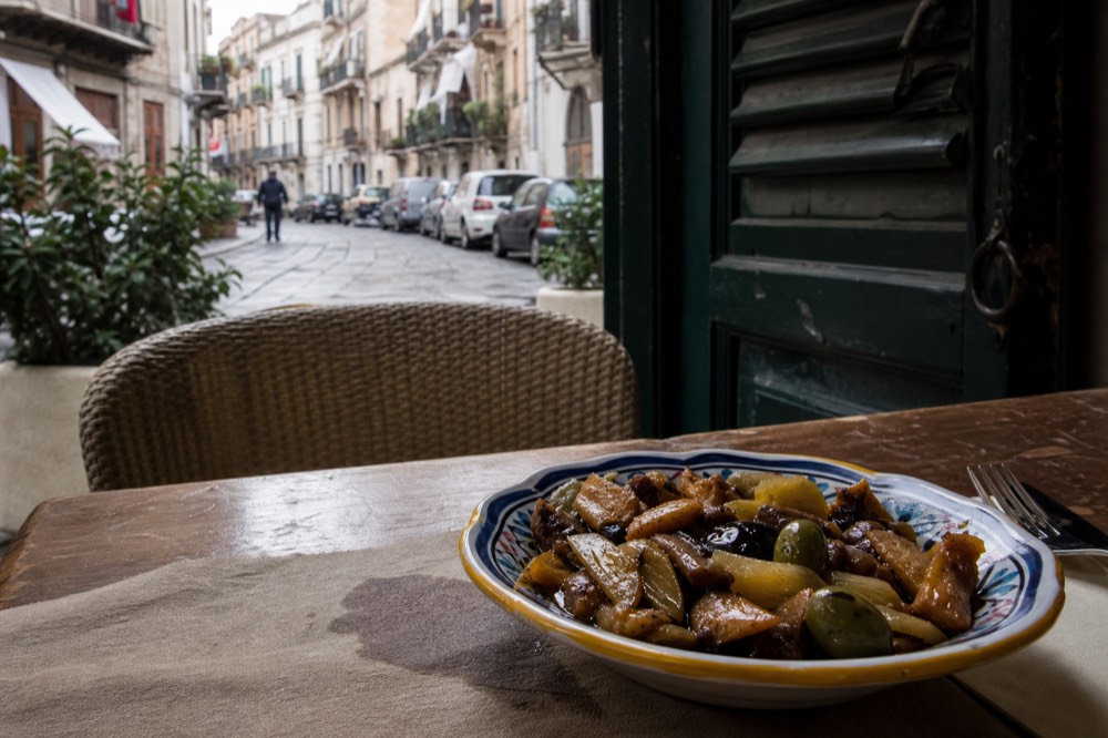 Caponata in a ceramic dish with celery, olives and fried aubergine glistening in sweet and sour sauce