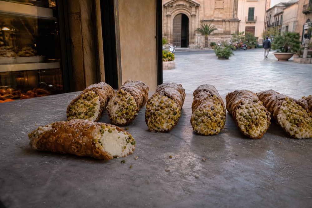 Cannoli filled with sheep's milk ricotta and pistachio crumbs arranged on a marble counter