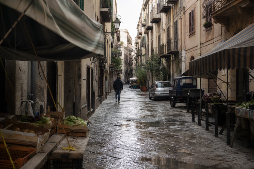 A historic market street with striped awnings, produce crates and old stone buildings in the morning light