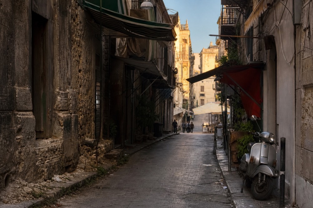 Narrow old street with market awnings and stone buildings in late afternoon light