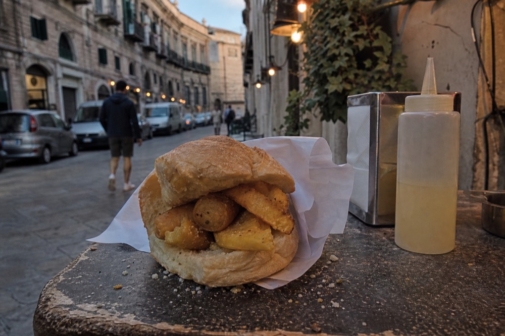 Chickpea fritters and potato croquettes in a fresh bread roll on a market counter