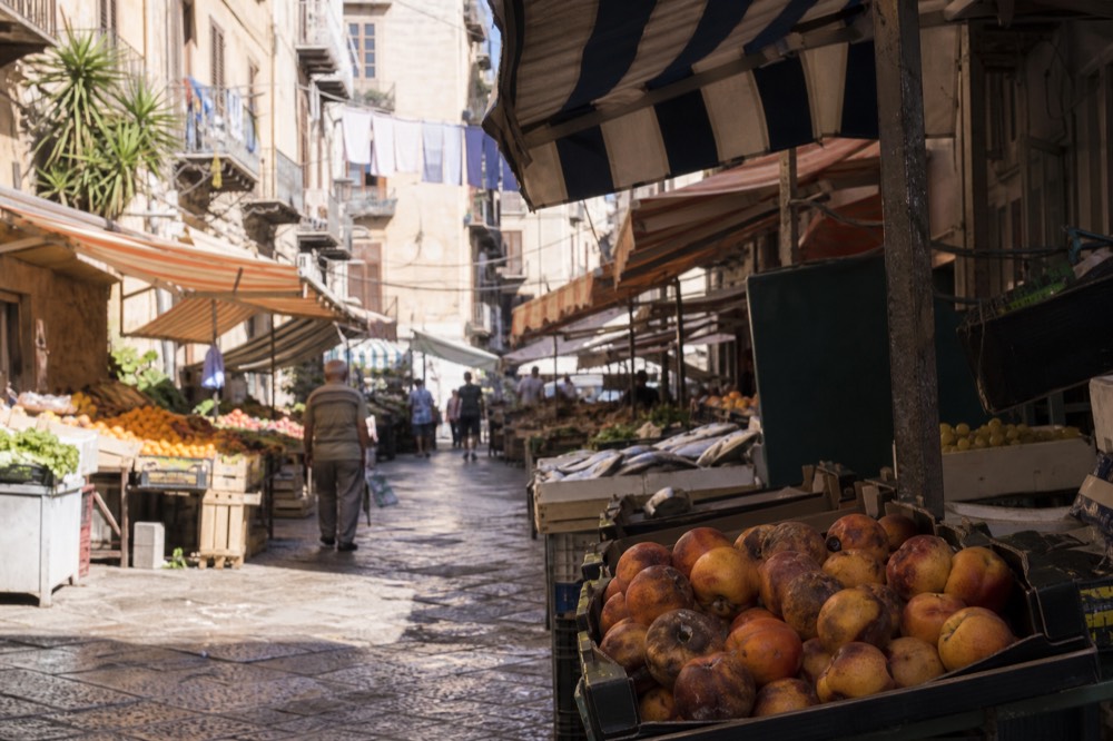 Busy morning street market with striped awnings, fruit stalls and shoppers