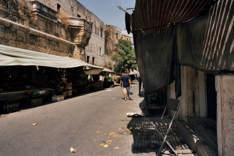 Strong summer light falling across a shaded market street in Palermo.