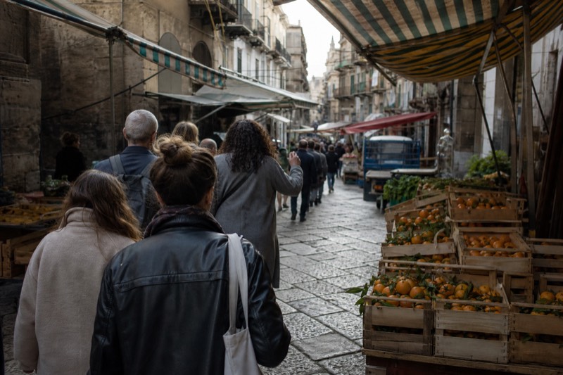 A small group following a guide through a Palermo market lane, seen from behind.